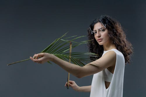 Woman in White Tank Top Holding Palm Leaves and Sticks