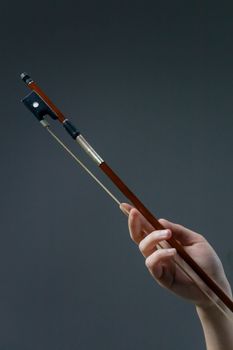 Artistic close-up of a hand holding a violin bow on a dark background.