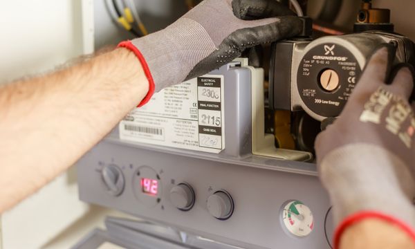 Geyser Repair & Replacement โ Close-up of hands adjusting a boiler system with precise instrumentation, showing maintenance work.