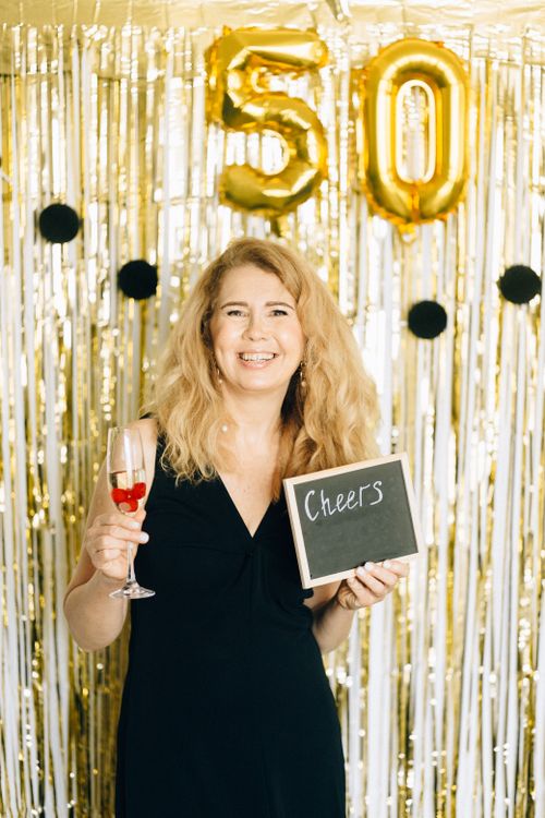 Free Woman in black dress celebrating her 50th birthday with a glass of wine and a cheers sign. Stock Photo