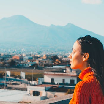 Profile of a woman in red sweater enjoying a serene outdoor view with mountains.
