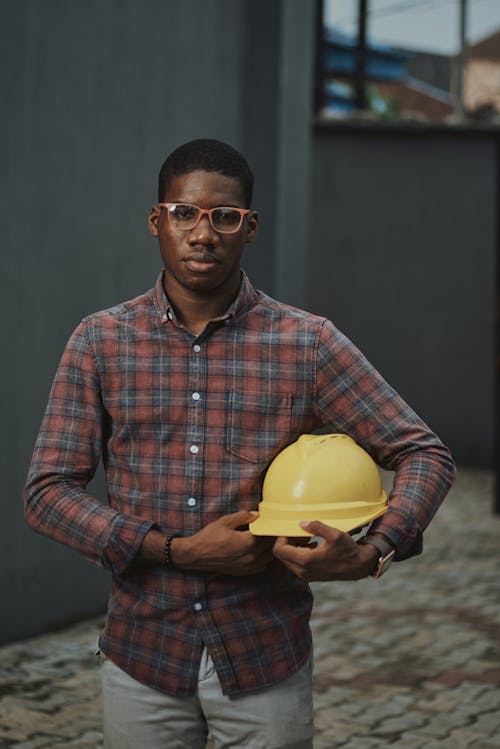 Free Man in Plaid Shirt Holding His Hard Hat while Looking at Camera Stock Photo