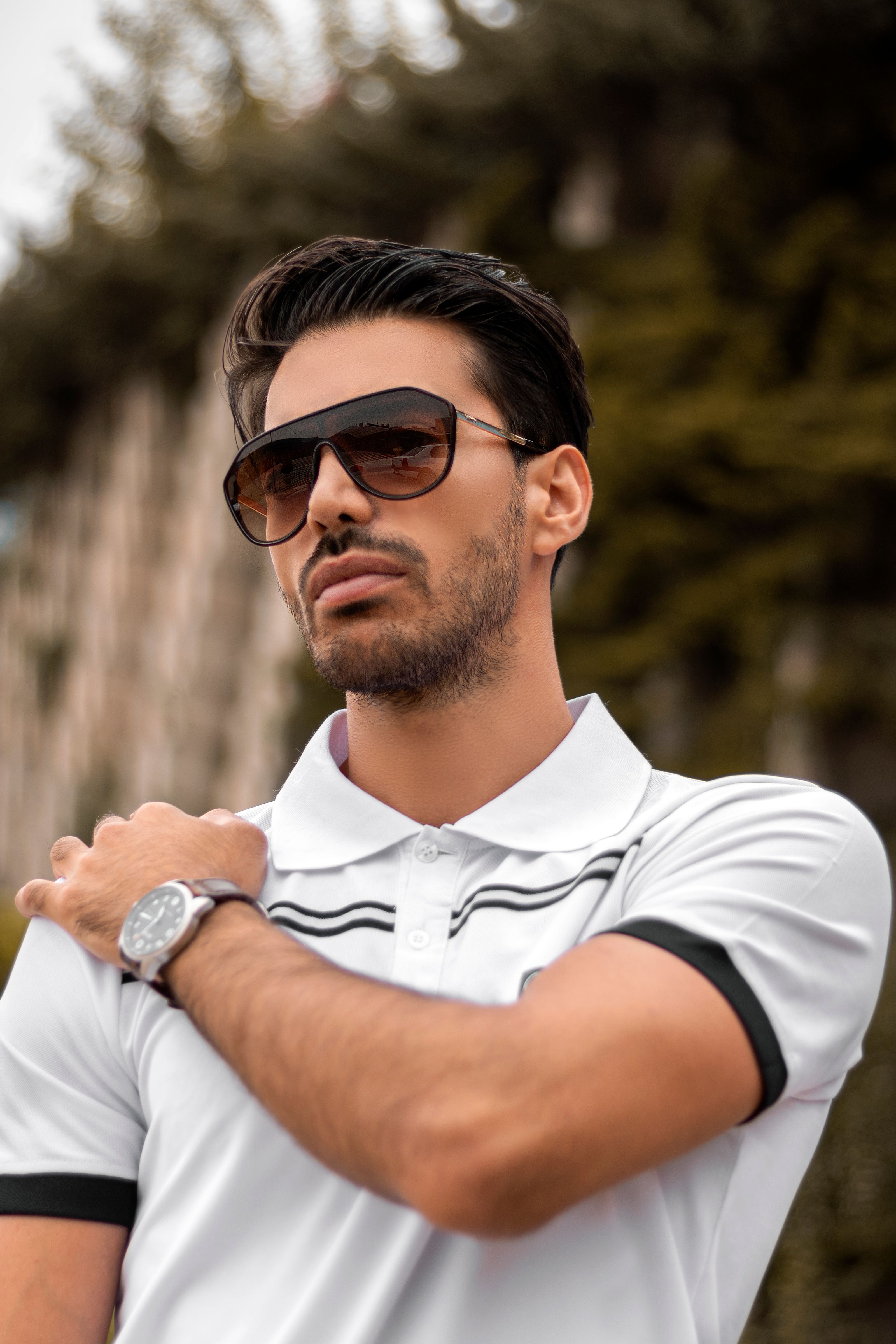 Homem estiloso de óculos de sol e camisa polo branca posando ao ar livre, exalando estilo moderno.