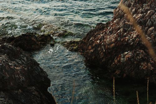 Free From above of rippling blue sea water washing rocky formations near grass on summer day Stock Photo