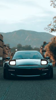 A modern black sports car parked on a scenic urban road with mountains in the background.