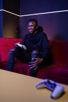 A young man is enjoying video gaming on a red sofa indoors, holding a game controller.