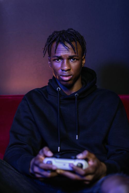 Free Young man in a black hoodie intensely focused on gaming indoors with a controller. Stock Photo