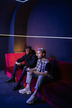 Two young men intently playing video games indoors on a stylish red sofa.