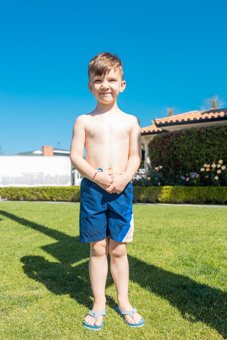 A Boy In Blue Shorts Standing On Green Grass Field