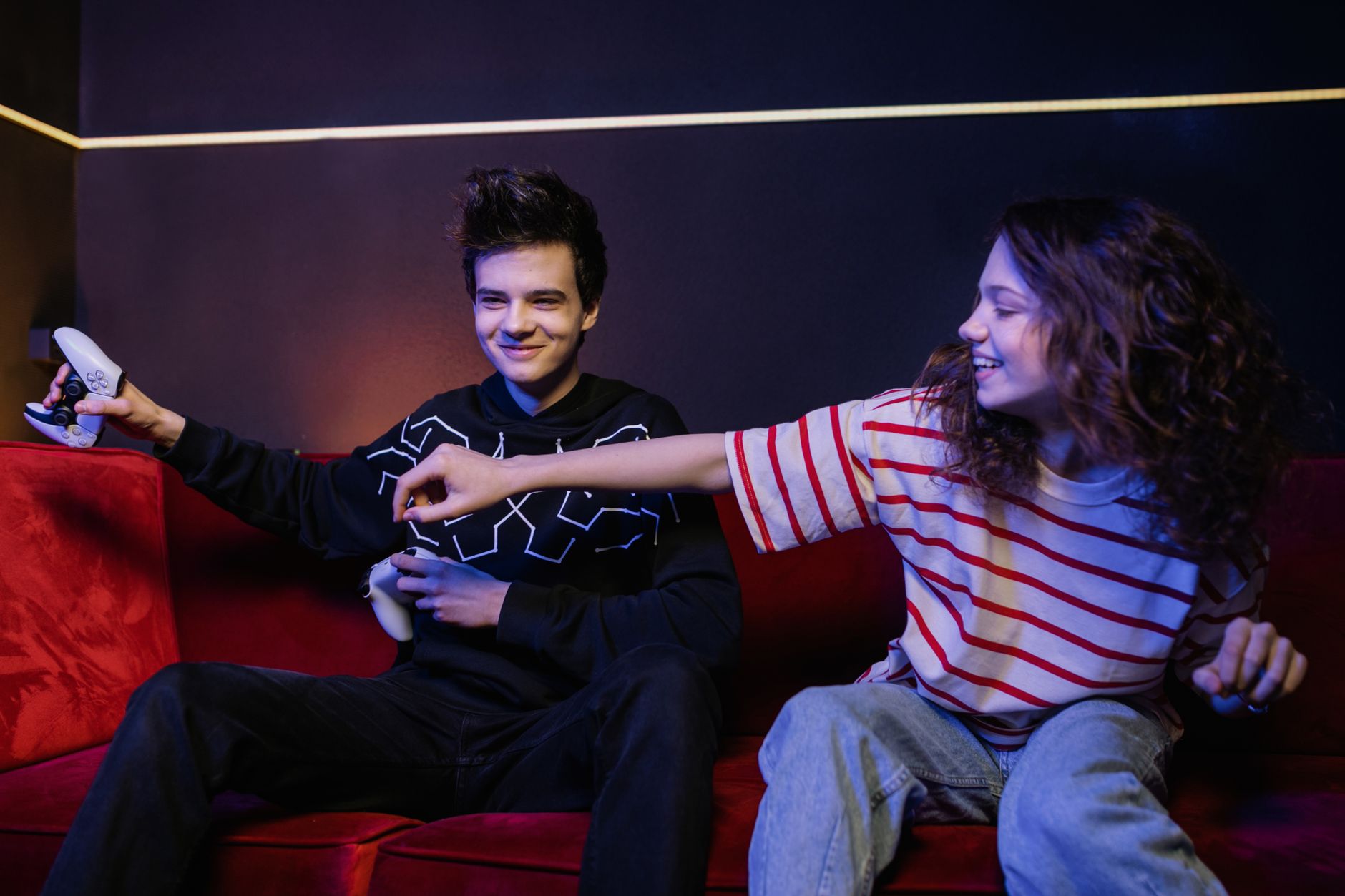 Two teenagers playing video games on sofa, smiling and having fun.