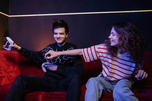 Two teenagers playing video games on sofa, smiling and having fun.