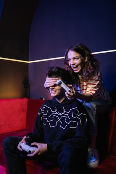 Teenagers enjoying video games together on a red sofa, expressing fun and companionship.