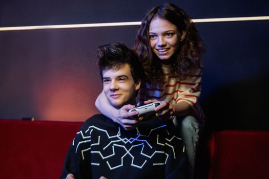 Two young adults having fun playing video games on a couch, smiling and holding a game controller.