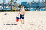 Boy in Blue Shorts Holding Red Bucket on Beach