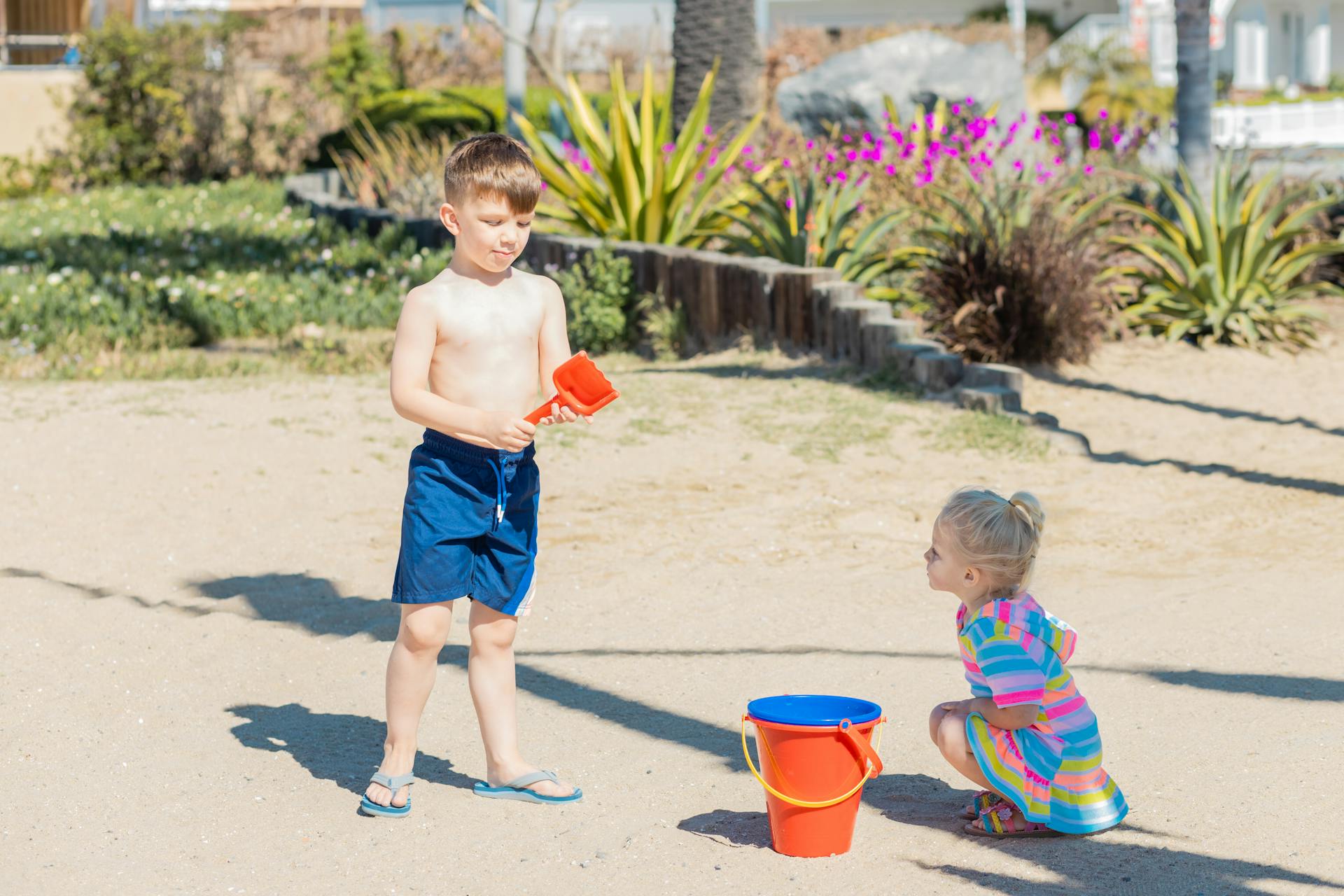 Two children enjoying a sunny day playing on the beach with buckets and sand toys.