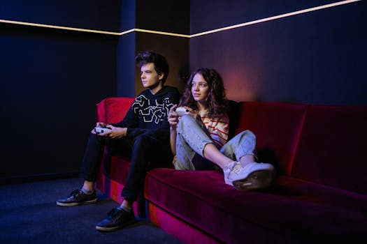 Two teenagers playing video games on a red couch in a modern indoor setting.
