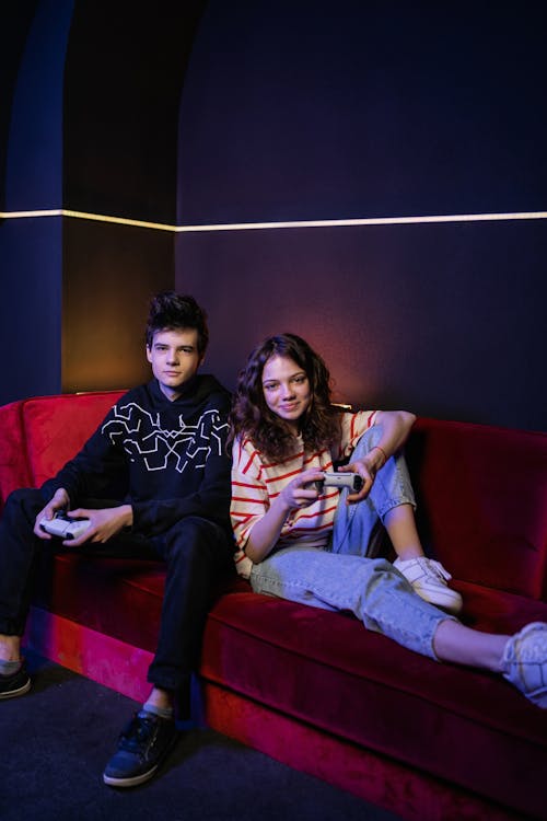 Boy and Girl Sitting on Red Couch while Holding Game Controllers