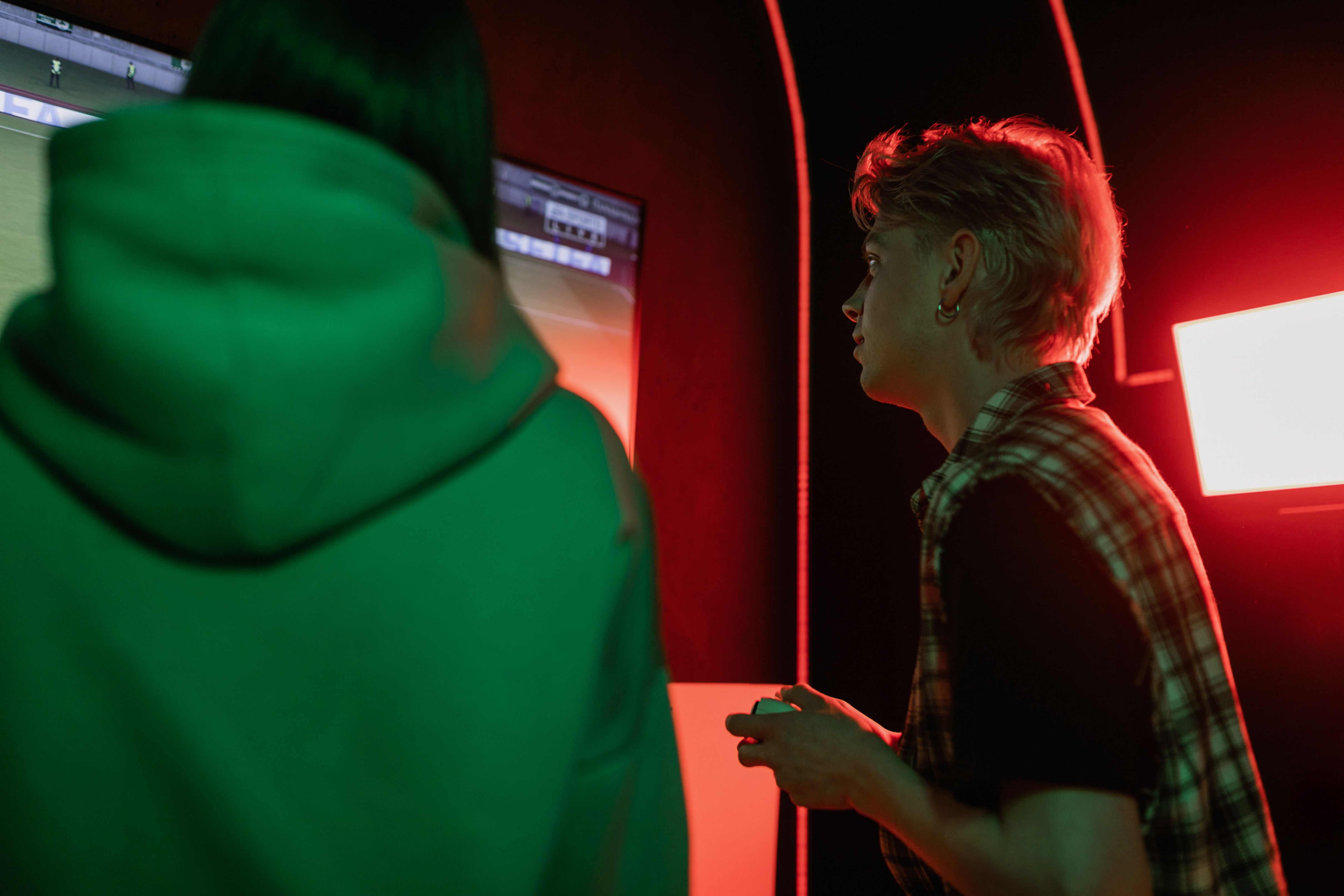 Two teenagers engrossed in a video game, illuminated by vivid lighting.