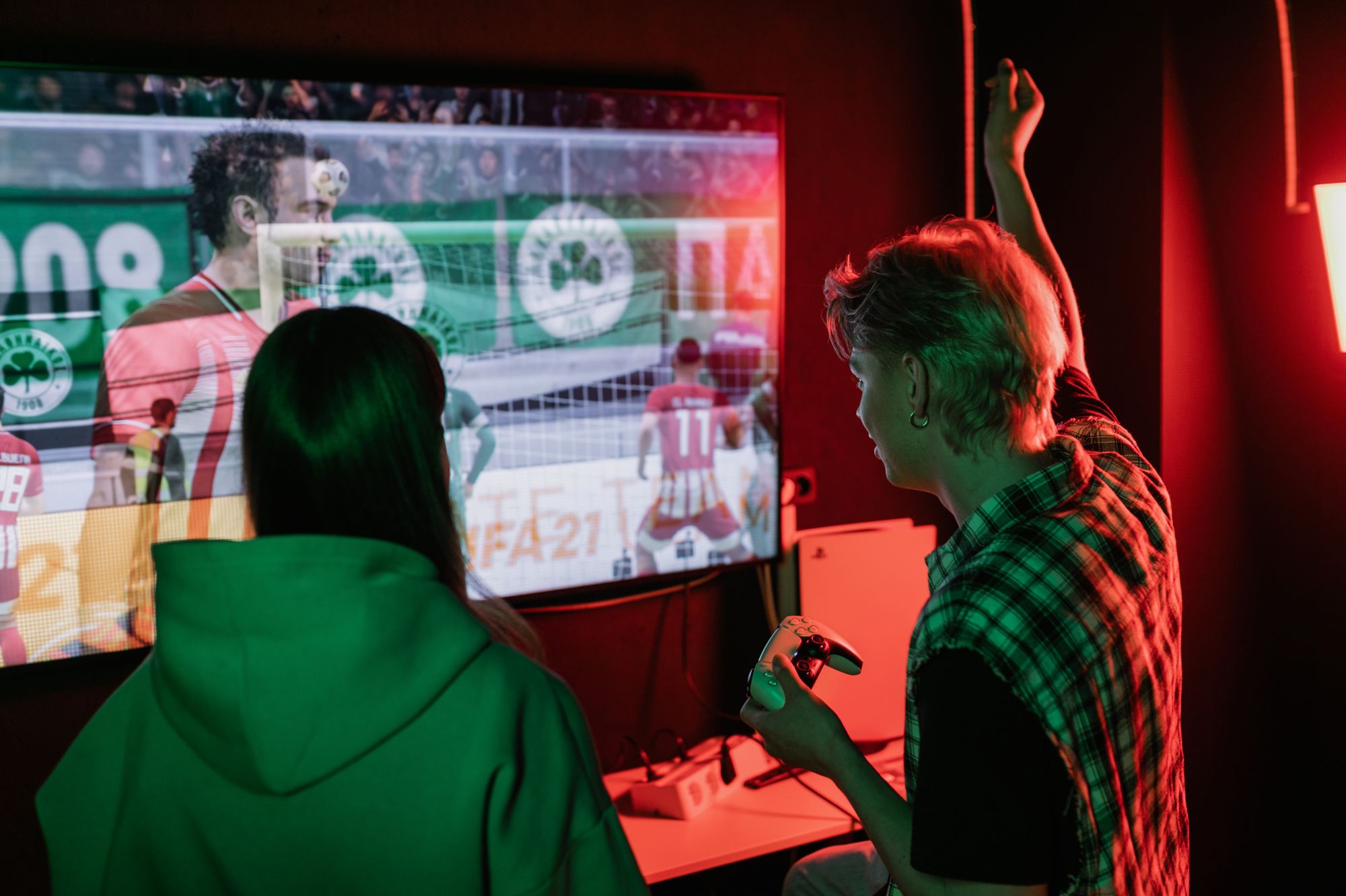Persona sosteniendo un control de videojuegos frente a una pantalla con un partido de futbol