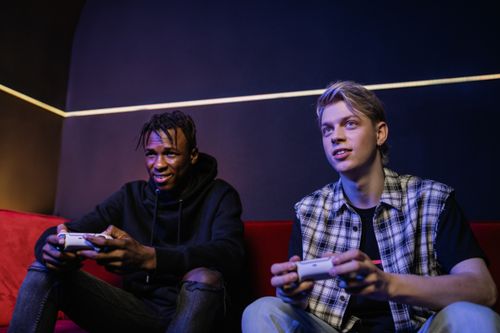 Free Two young men playing video games and enjoying leisure time on a couch indoors. Stock Photo
