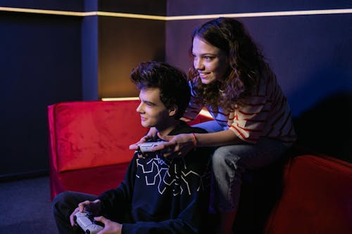 Boy and Girl Sitting on Red Couch while Playing Video Games