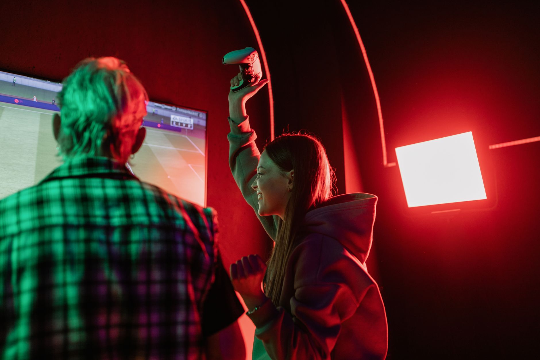 gamer celebrating a virtual touchdown while a football statistics dashboard glows on a second monitor