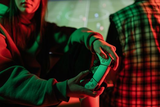 A gamer holding a controller while playing a video game indoors with colorful lighting.