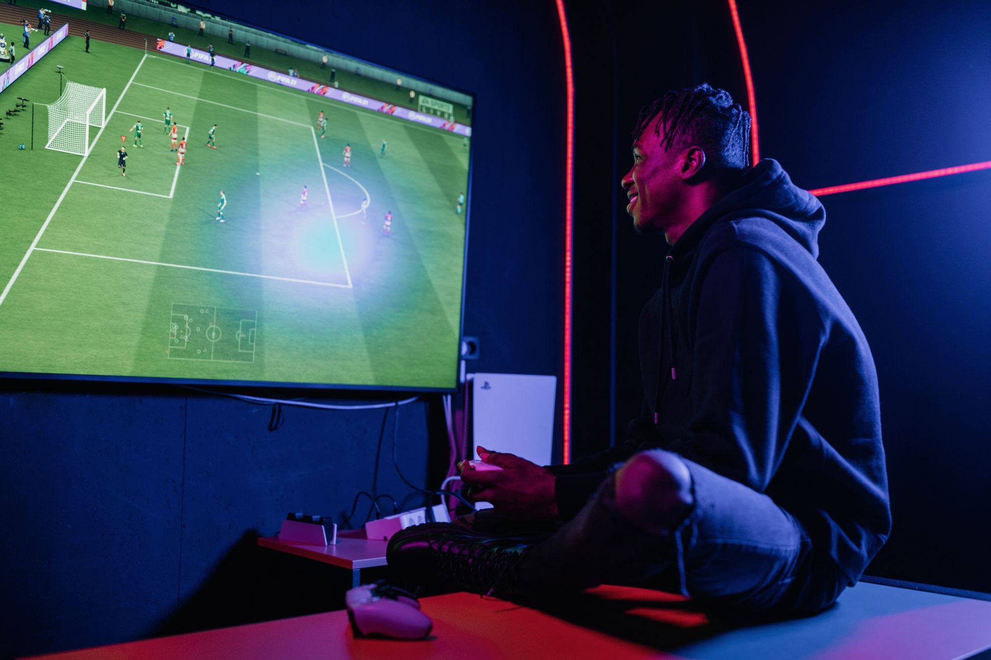 Manos sosteniendo un control de videojuego frente a una pantalla con un partido de futbol virtual
