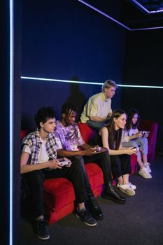 A vibrant group of teenagers playing video games on a red sofa in a modern gaming room.