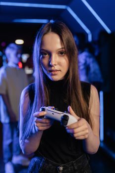 Teen girl focused on gaming with a controller in a neon-lit room.