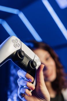 Close-up of a person holding a game controller with blue neon lights in the background.