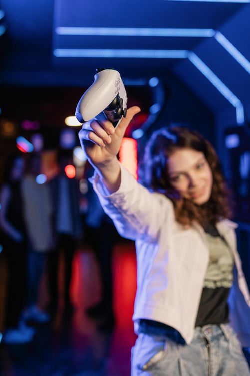 Free A young woman energetically holds a game controller in a vibrant neon-lit arcade setting. Perfect for gaming concepts. Stock Photo