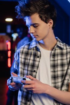 A teenage boy focused while holding a game controller in a dimly lit room.