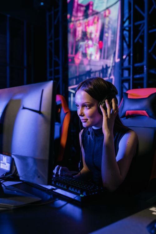 Free A woman gamer with a headset deeply focused on playing video games in an esports arena. Stock Photo