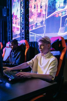 Two young men intensely gaming at an esports event with neon-lit screens.