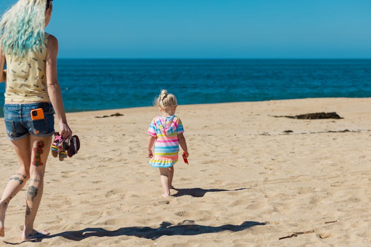 Mother And Daughter Walking On Beach Shore