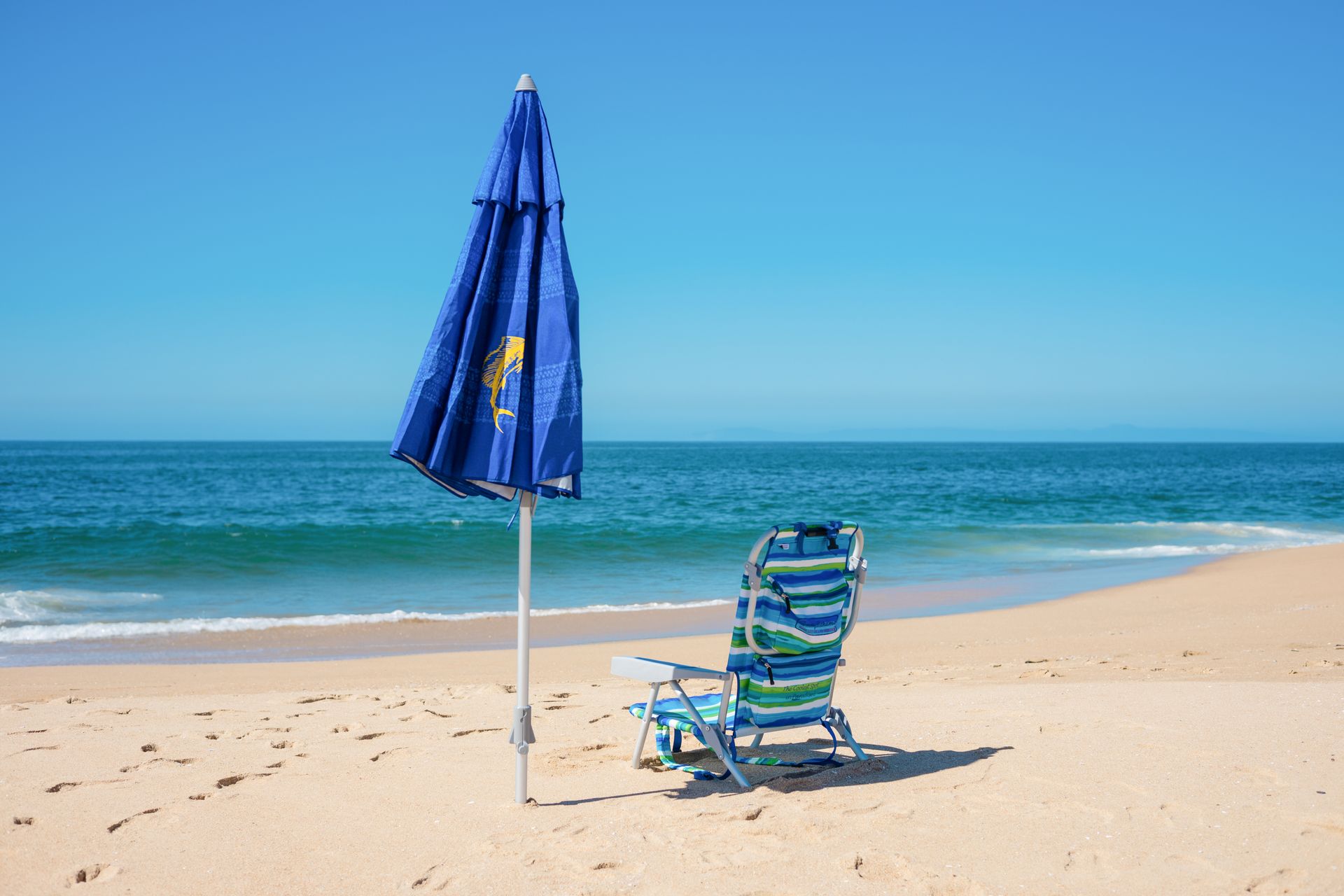 A tranquil beach setting with a chair and umbrella under a clear blue sky.