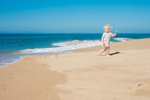 Free A young girl confidently plays on a sunny beach with clear blue skies and gentle waves. Stock Photo