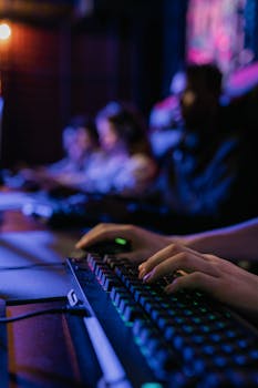 Close-up of hands on keyboard during a multiplayer gaming session in dimly lit room.