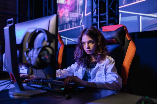 Woman in White Long Sleeve Shirt Sitting on Chair using Black Computer Keyboard