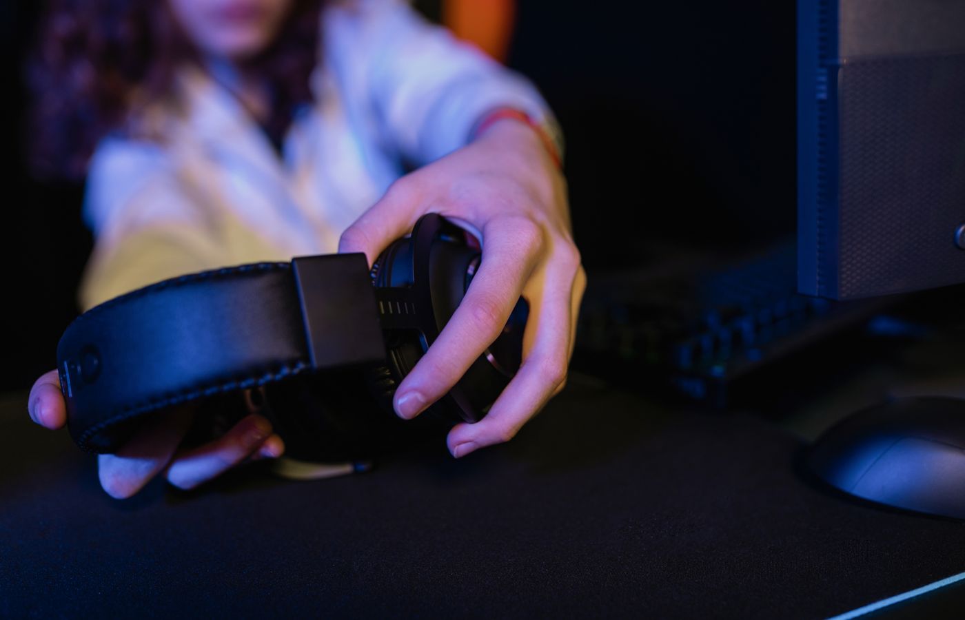 Close-up of a person holding a gaming headset in a computer setup.