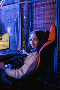 Smiling woman playing video games on a computer with a gaming headset in a stylish setup.