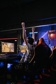 A teenage boy raises his hands in victory while playing video games in an esports arena.