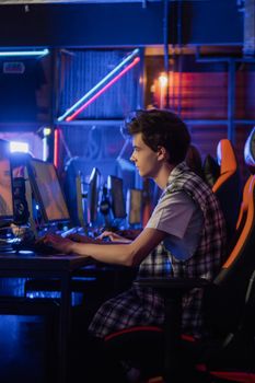 Side view of a teenager gaming intensely in a neon-lit room, enhancing the immersive experience.