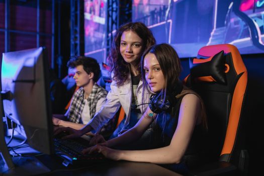 Three teenagers gaming intensely at an esports arena with computers and gaming chairs.