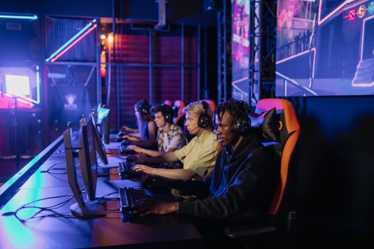 A group of focused teenagers playing in an esports tournament setup with gaming chairs and monitors.