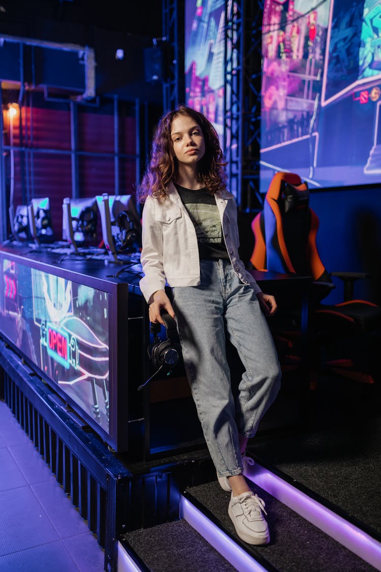 A Woman In White Jacket And Denim Pants Standing While Leaning On The Table