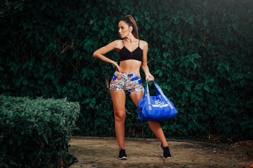 Sportswoman with sports bag standing against green plants