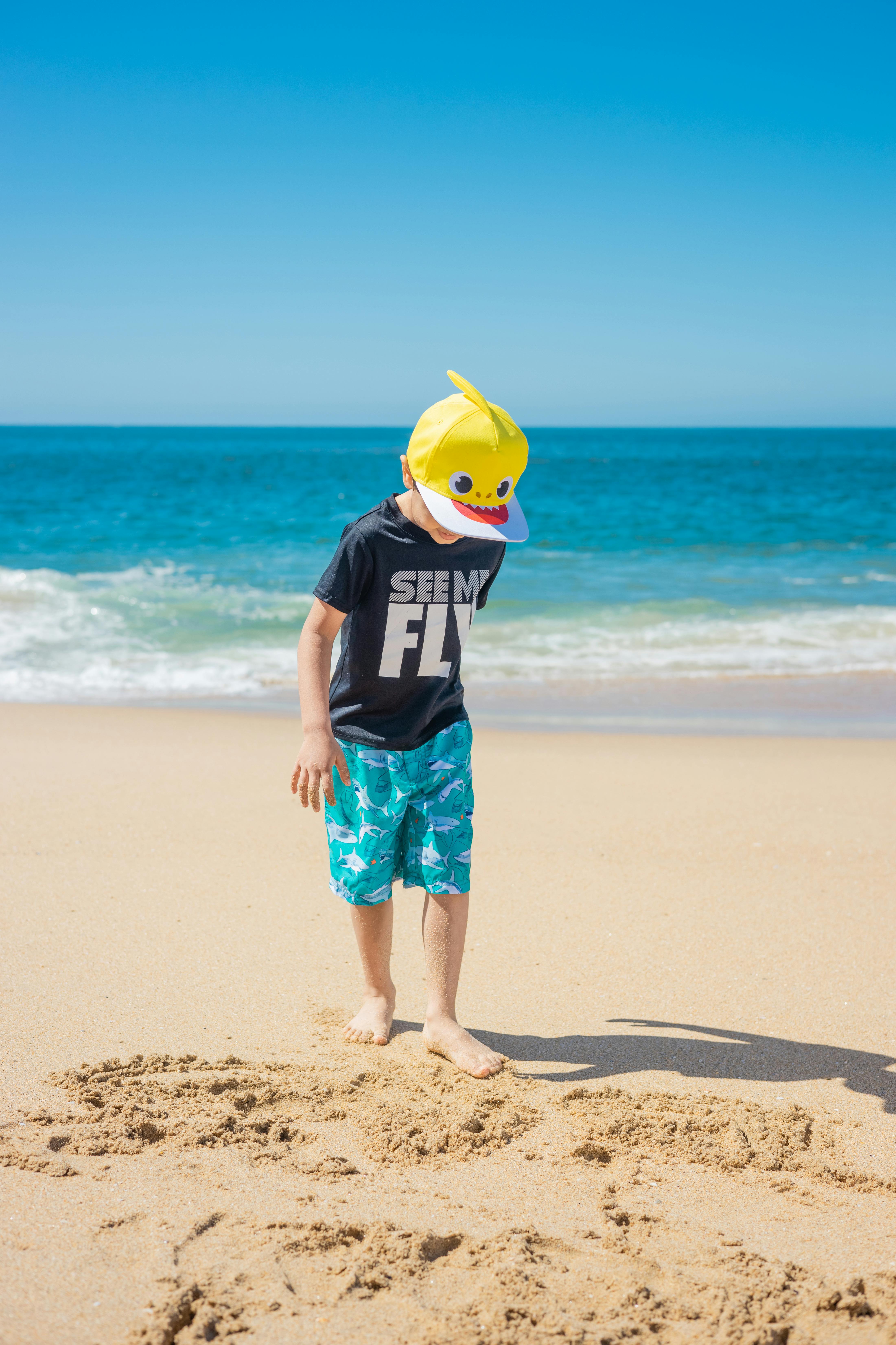 一个戴着黄色鲨鱼帽的小男孩在海边的沙滩上享受阳光明媚的一天
