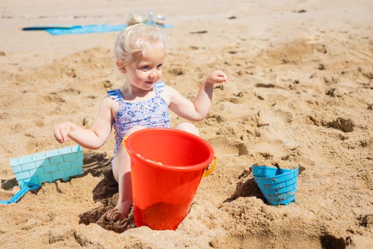 A Young Girl Sitting On The Beach Sand While Playing Her Toys